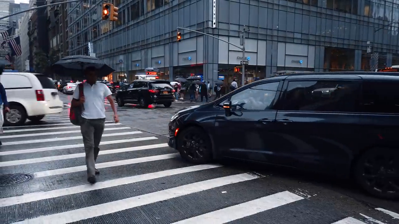 Appendix dataset sample 7637_6 showing a city crosswalk with a person holding an umbrella and a black minivan.
